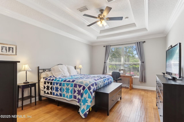 bedroom featuring visible vents, light wood-style flooring, ornamental molding, a textured ceiling, and a raised ceiling