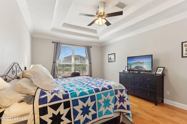 bedroom with visible vents, ornamental molding, light wood-style floors, a textured ceiling, and a raised ceiling