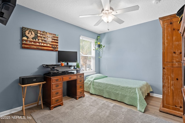 bedroom featuring ceiling fan, light wood-style floors, baseboards, and a textured ceiling