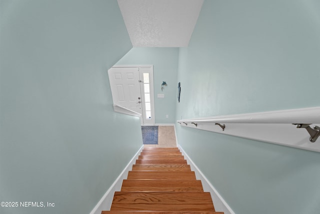 staircase featuring vaulted ceiling, a textured ceiling, baseboards, and wood finished floors