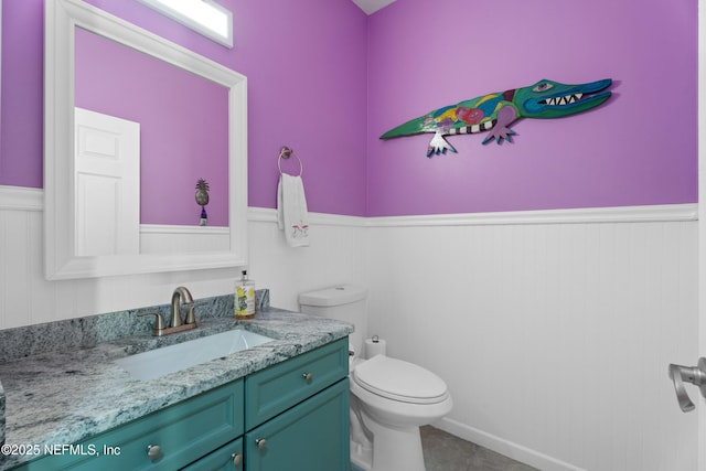 bathroom with tile patterned floors, wainscoting, vanity, and toilet