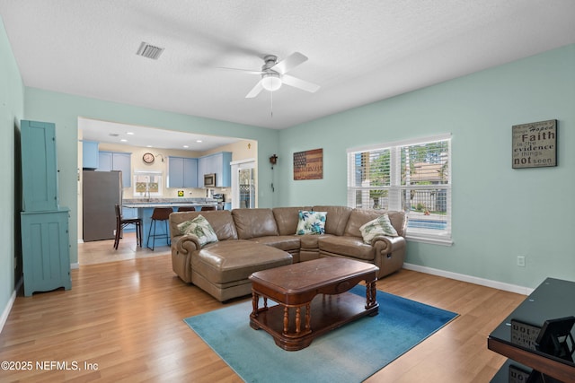 living area featuring baseboards, a textured ceiling, ceiling fan, and light wood finished floors