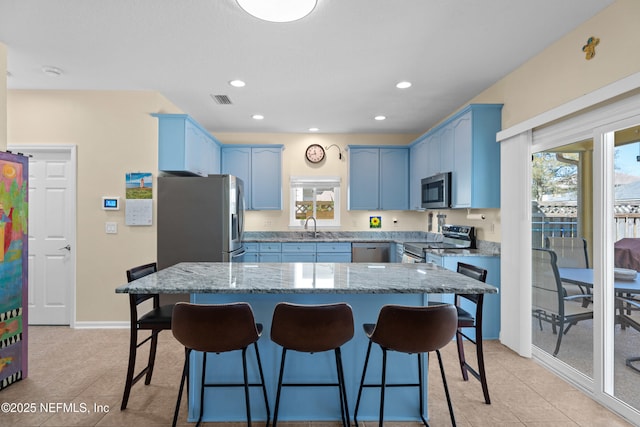 kitchen with blue cabinetry, light stone countertops, appliances with stainless steel finishes, and a sink