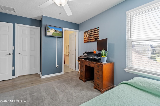 carpeted bedroom featuring a textured ceiling, multiple windows, visible vents, and ceiling fan