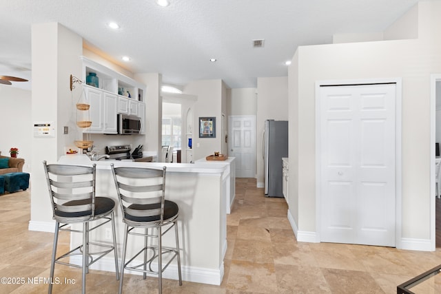 kitchen with visible vents, a breakfast bar, a peninsula, appliances with stainless steel finishes, and white cabinetry