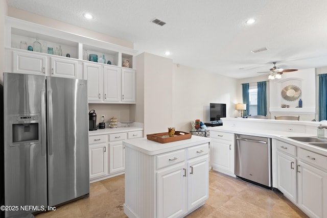 kitchen featuring visible vents, a kitchen island, light countertops, stainless steel appliances, and white cabinetry