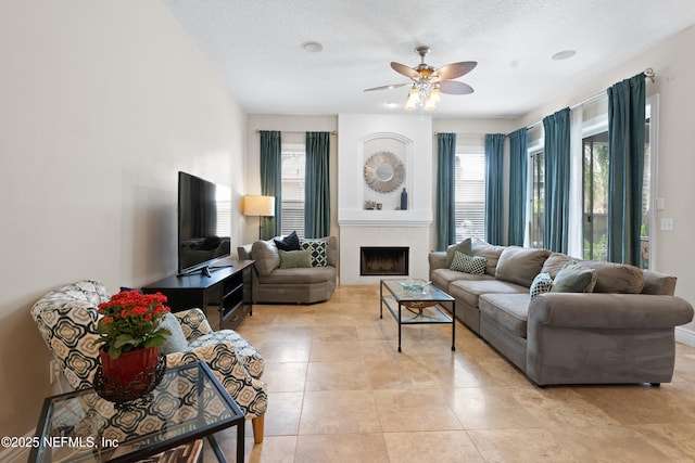 living room with light tile patterned floors, a fireplace, a textured ceiling, and a ceiling fan