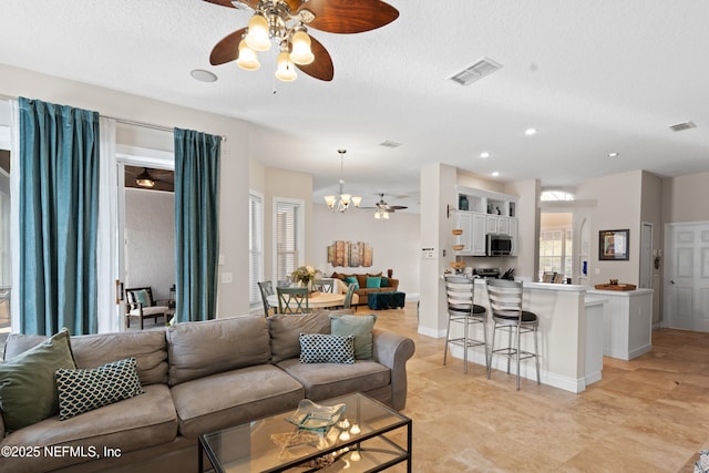 living area featuring ceiling fan with notable chandelier, visible vents, and a textured ceiling