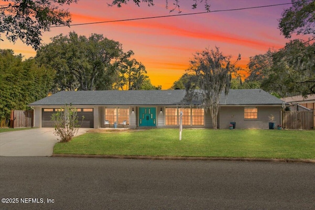 ranch-style house featuring concrete driveway, an attached garage, a lawn, and fence