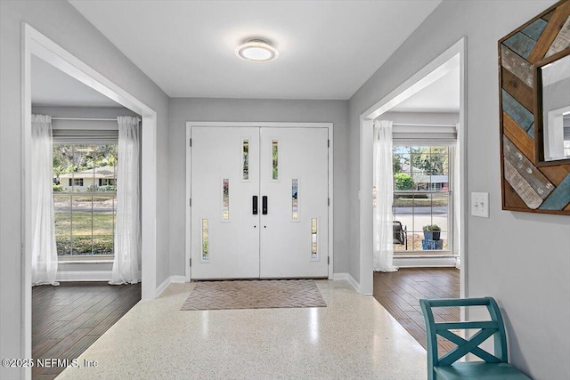 foyer entrance featuring a wealth of natural light, speckled floor, and baseboards