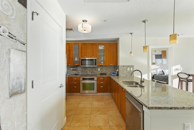 kitchen with visible vents, a peninsula, a sink, appliances with stainless steel finishes, and brown cabinets