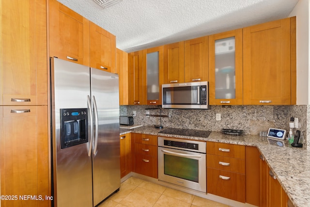 kitchen with brown cabinetry, light tile patterned floors, and appliances with stainless steel finishes