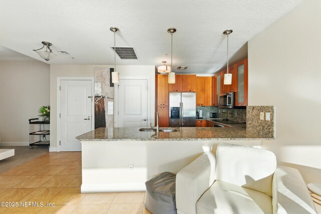 kitchen with visible vents, a sink, stainless steel appliances, a peninsula, and brown cabinetry