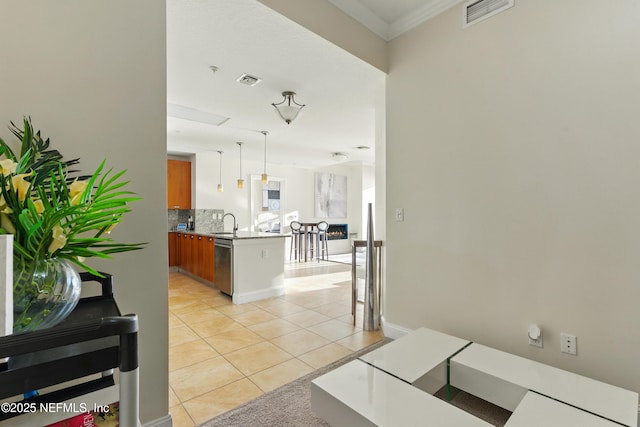 kitchen with light tile patterned floors, a peninsula, a sink, stainless steel dishwasher, and brown cabinets