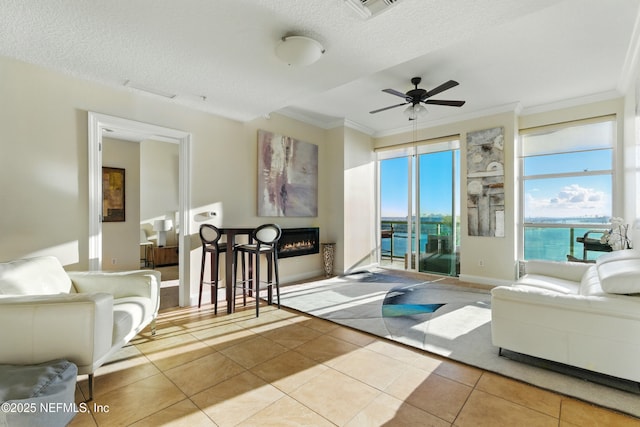 living area with a glass covered fireplace, tile patterned floors, crown molding, and a ceiling fan