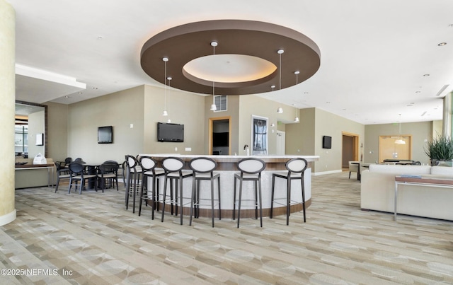 kitchen with a breakfast bar area, baseboards, visible vents, hanging light fixtures, and light carpet