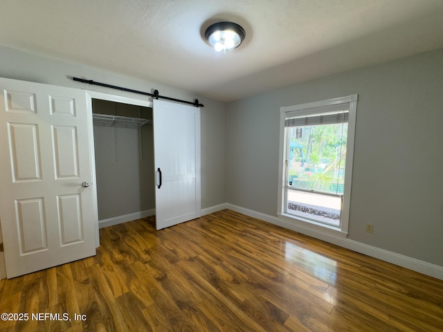 unfurnished bedroom featuring a barn door, baseboards, a closet, and wood finished floors