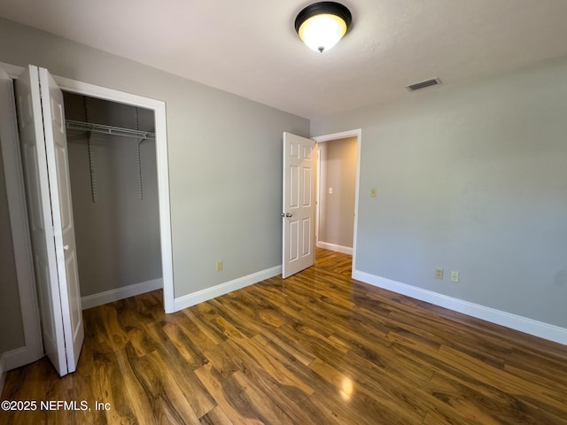 unfurnished bedroom featuring visible vents, baseboards, dark wood-type flooring, and a closet