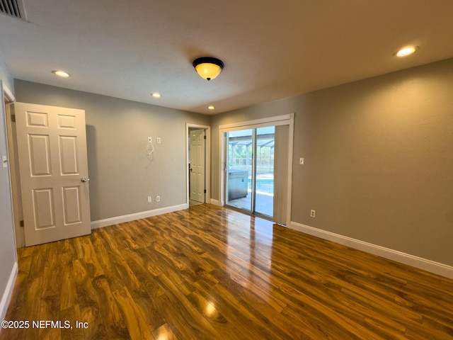 empty room with dark wood finished floors, visible vents, and baseboards