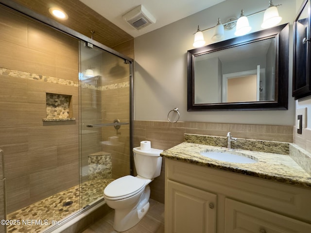 full bath with visible vents, toilet, tile walls, a shower stall, and vanity