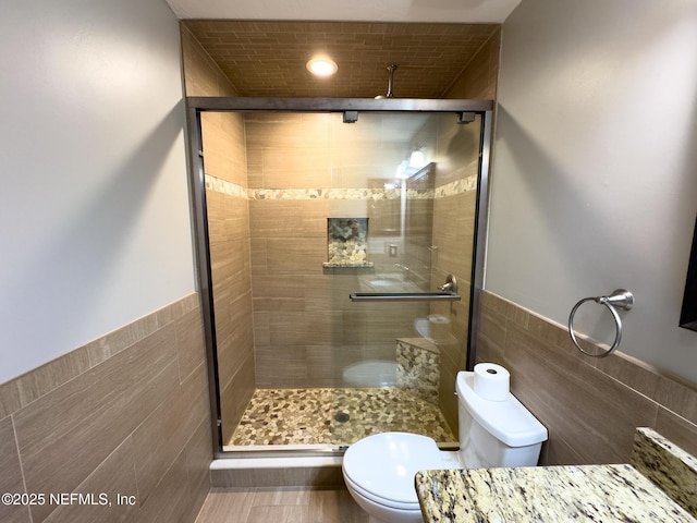 full bath with a wainscoted wall, tile walls, toilet, and a stall shower