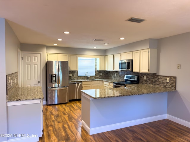 kitchen with visible vents, stone counters, a peninsula, a sink, and stainless steel appliances