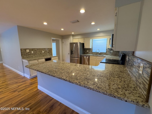 kitchen featuring light stone counters, dark wood-style floors, a peninsula, a sink, and appliances with stainless steel finishes