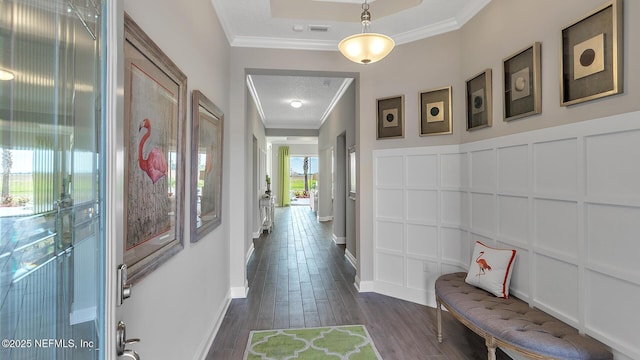 hall with crown molding, a decorative wall, baseboards, and dark wood-style flooring