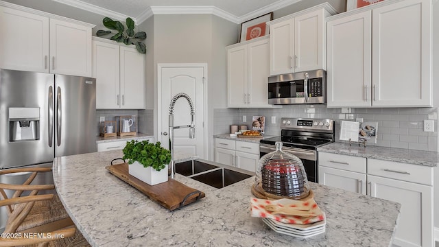 kitchen with a breakfast bar, ornamental molding, stainless steel appliances, white cabinetry, and backsplash