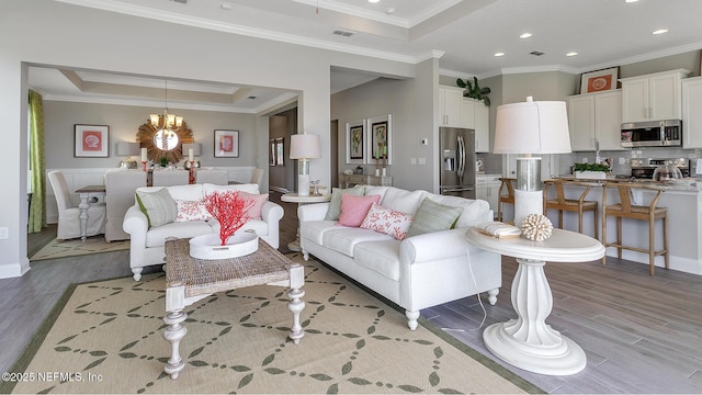 living area with an inviting chandelier, a tray ceiling, and light wood finished floors