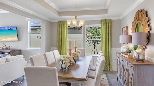 dining area featuring an inviting chandelier, a raised ceiling, light wood-type flooring, and ornamental molding