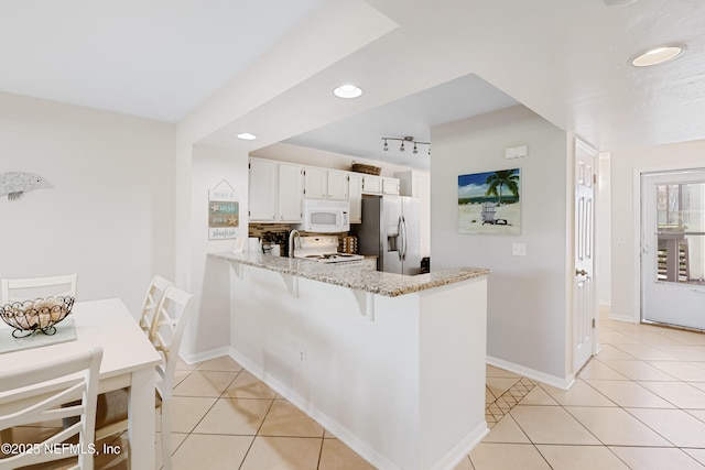 kitchen featuring light tile patterned floors, light stone counters, white appliances, and a peninsula