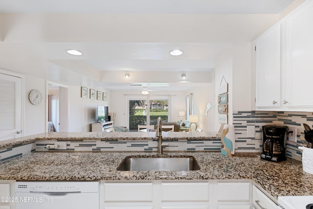 kitchen with backsplash, open floor plan, white dishwasher, white cabinets, and a sink