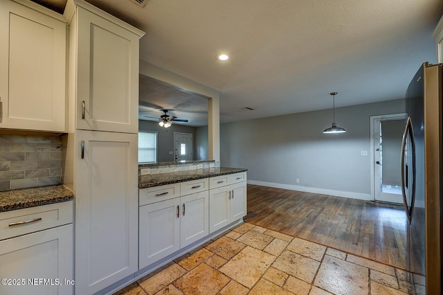 kitchen featuring tasteful backsplash, stone tile floors, freestanding refrigerator, white cabinets, and baseboards