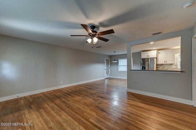 unfurnished living room with dark wood finished floors, a ceiling fan, visible vents, and baseboards