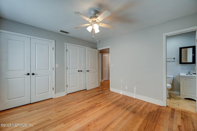 unfurnished bedroom featuring visible vents, two closets, baseboards, ensuite bathroom, and light wood-style floors