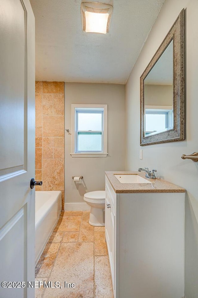 bathroom featuring baseboards, toilet, vanity, stone tile flooring, and a textured ceiling