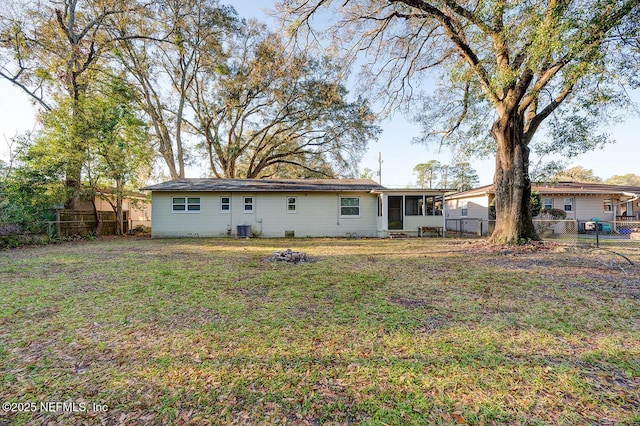 rear view of property featuring central air condition unit, a lawn, a fenced backyard, and a sunroom