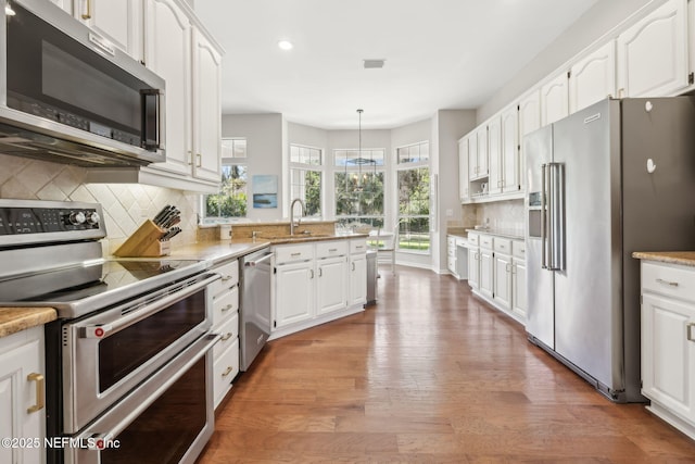 kitchen featuring a peninsula, decorative backsplash, appliances with stainless steel finishes, white cabinetry, and light wood-type flooring