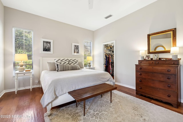 bedroom featuring visible vents, baseboards, a walk in closet, and wood finished floors