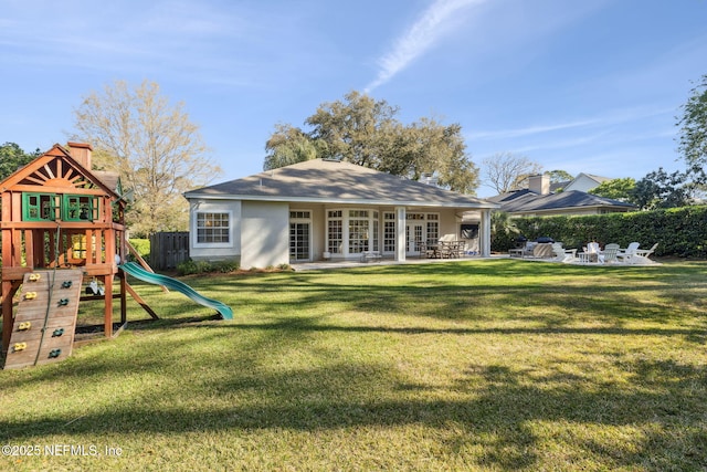 back of house featuring a patio area, a lawn, a playground, and stucco siding