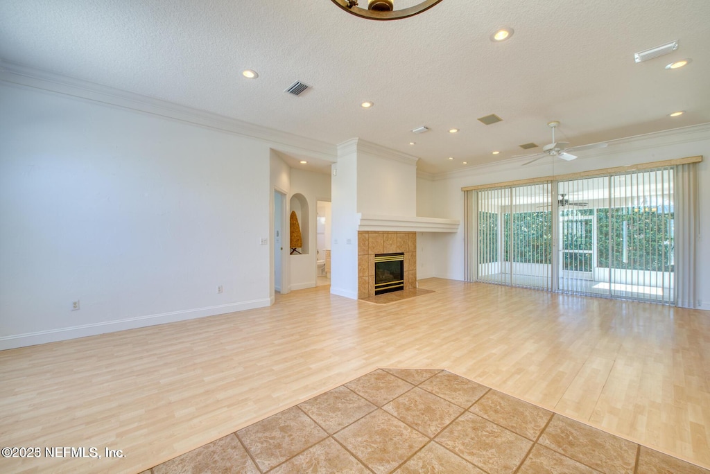 unfurnished living room with light wood-style flooring, ornamental molding, a ceiling fan, a textured ceiling, and a fireplace