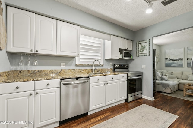 kitchen featuring light stone countertops, appliances with stainless steel finishes, dark wood-style floors, white cabinets, and a sink