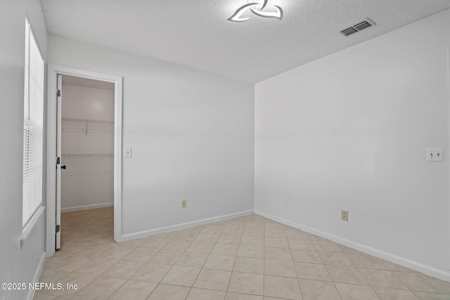 unfurnished bedroom with visible vents, a walk in closet, a textured ceiling, a closet, and baseboards