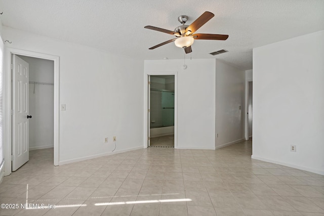 unfurnished bedroom with a spacious closet, visible vents, light tile patterned floors, ensuite bath, and a textured ceiling