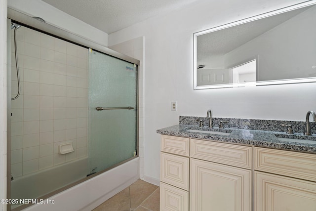 bathroom with a textured ceiling, tile patterned flooring, shower / bath combination with glass door, and a sink