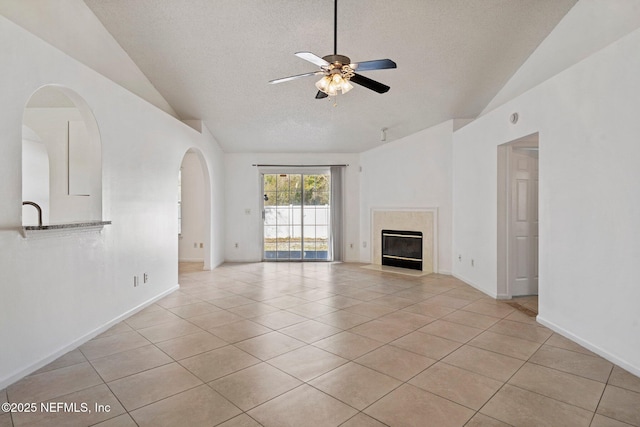 unfurnished living room with light tile patterned floors, a ceiling fan, arched walkways, a high end fireplace, and vaulted ceiling