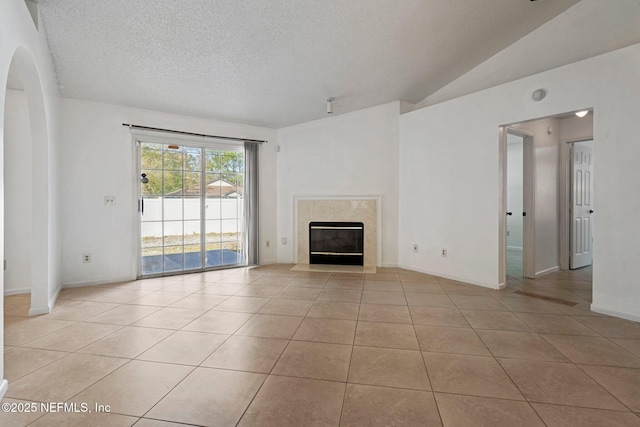 unfurnished living room featuring a textured ceiling, arched walkways, a fireplace, light tile patterned floors, and vaulted ceiling