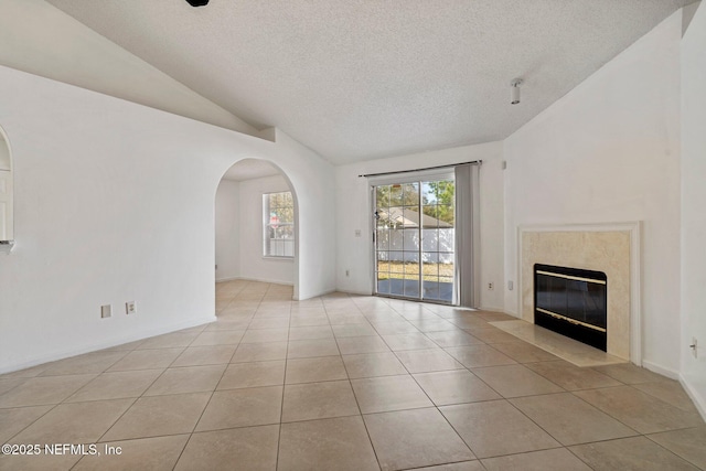 unfurnished living room with a fireplace, arched walkways, tile patterned flooring, vaulted ceiling, and a textured ceiling