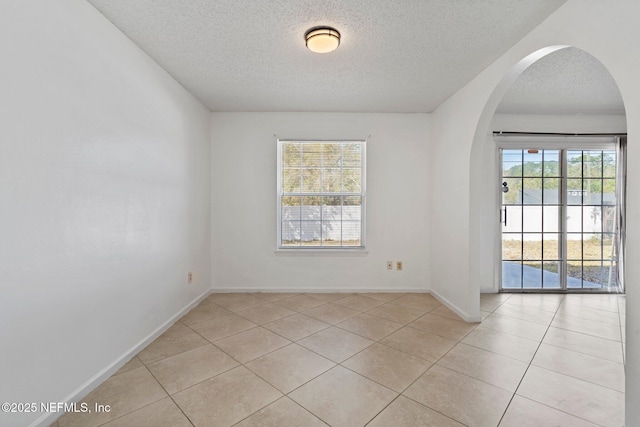 unfurnished room featuring light tile patterned flooring, baseboards, arched walkways, and a textured ceiling